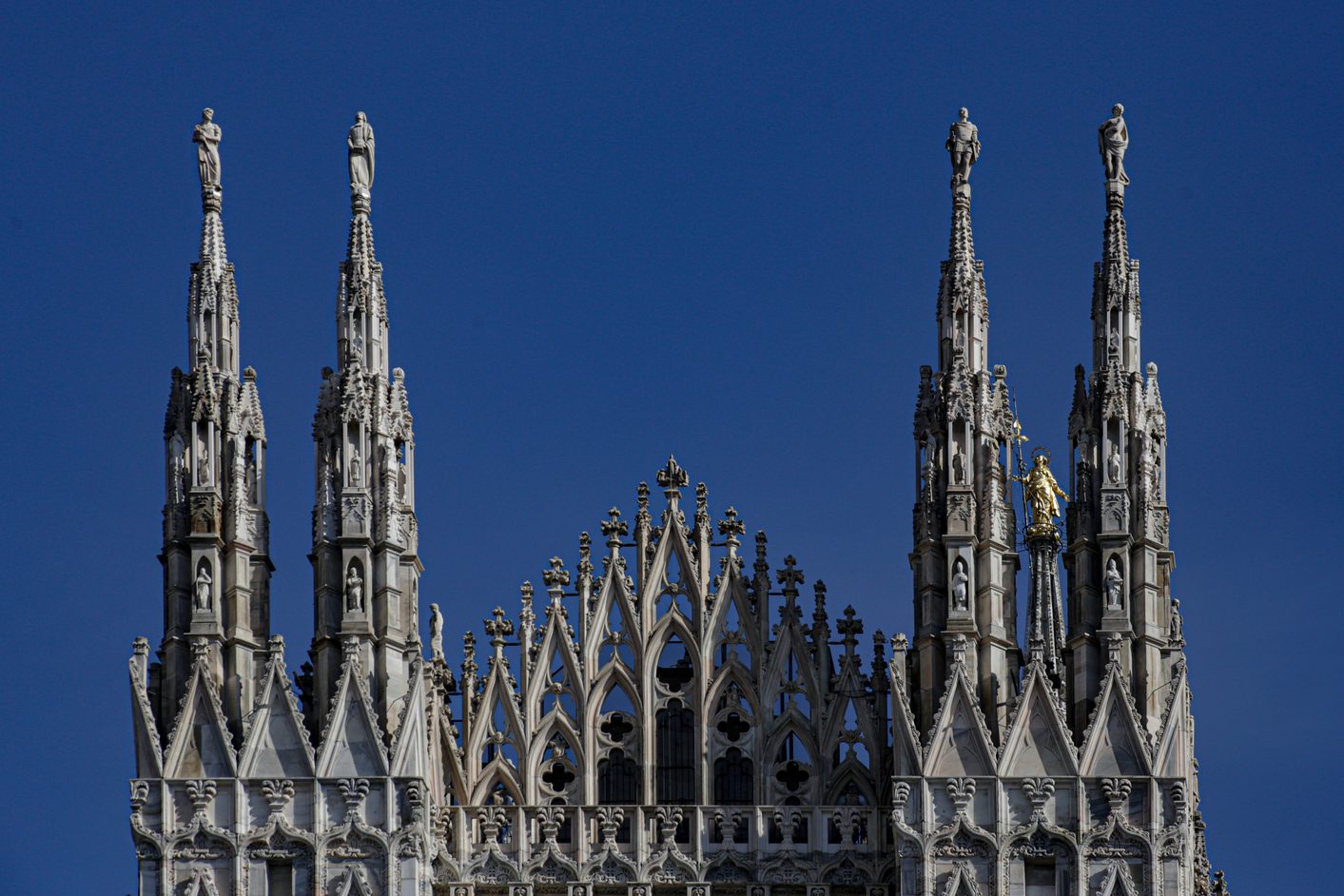 Gothic spires topped with statues on Milan Cathedral against a deep blue sky