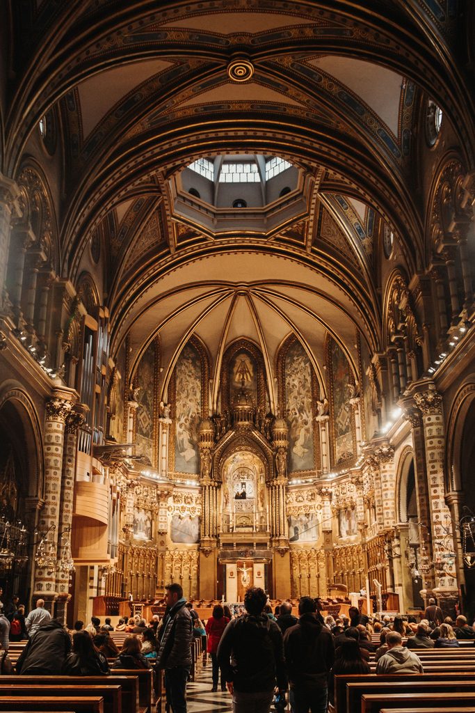 The dark, richly gilded interior of the basilica of Montserrat, with lamps hanging before the high altar