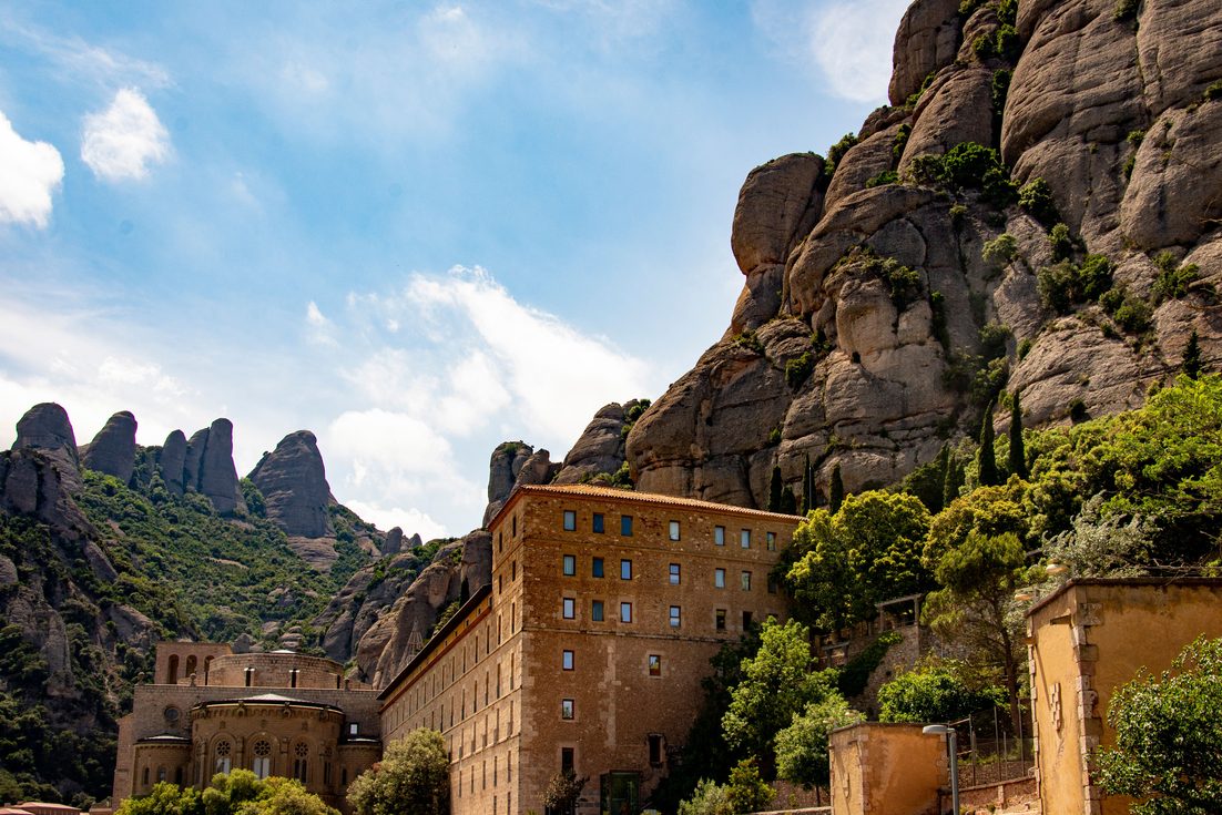 The tall buildings of Montserrat monastery against towering rounded rock formations and blue sky