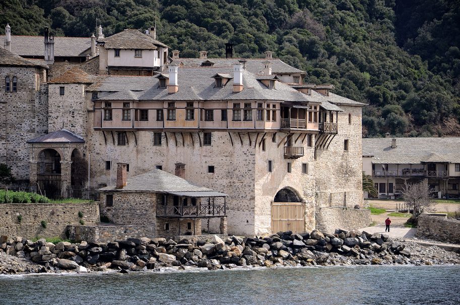 A stone monastery with a tower and wooden balconies right at the water's edge on Mount Athos