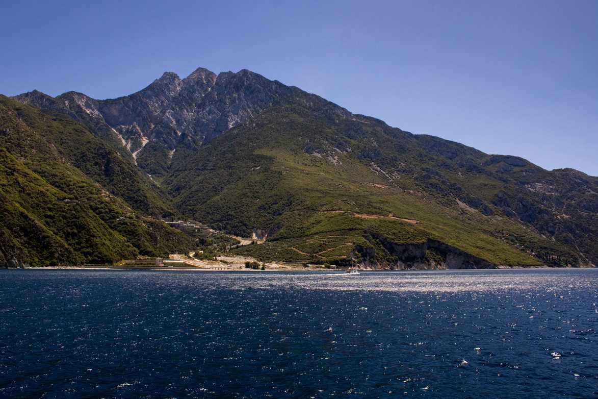 The bare limestone peak of Mount Athos above forested ridges and the sea under a deep blue sky