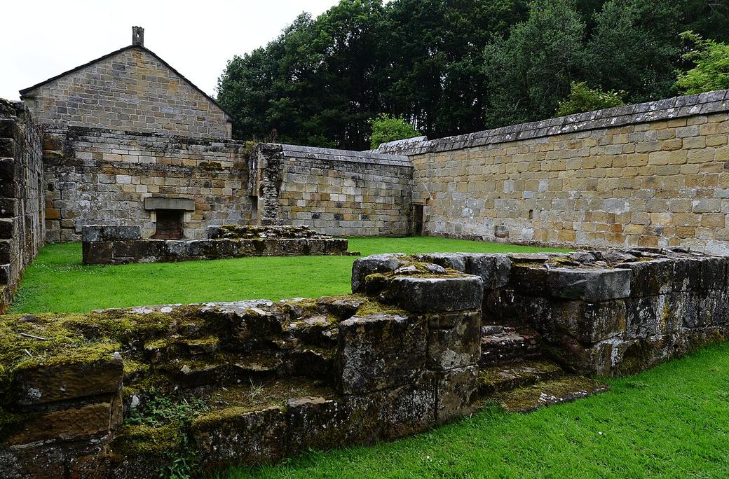 The low walls of the monks' cells around the great cloister at Mount Grace, with the reconstructed cell beyond
