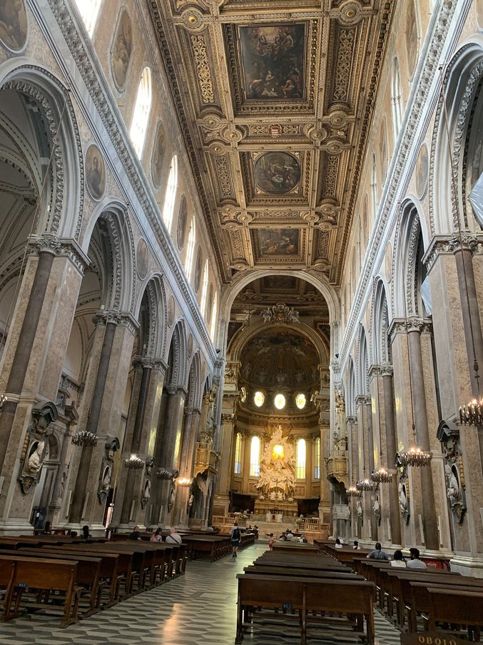 The long nave of Naples Cathedral with a gilded coffered ceiling, painted panels above the arcades and the apse at the far end