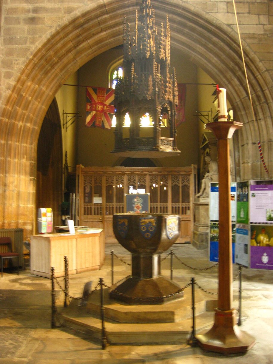 The medieval stone font of Newcastle Cathedral under its tall carved wooden canopy