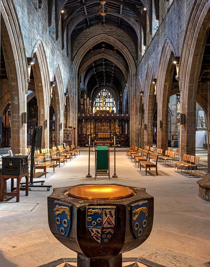 The nave of Newcastle Cathedral, open and free of pews, looking east to the quire, with a stone font carved with coats of arms in the foreground