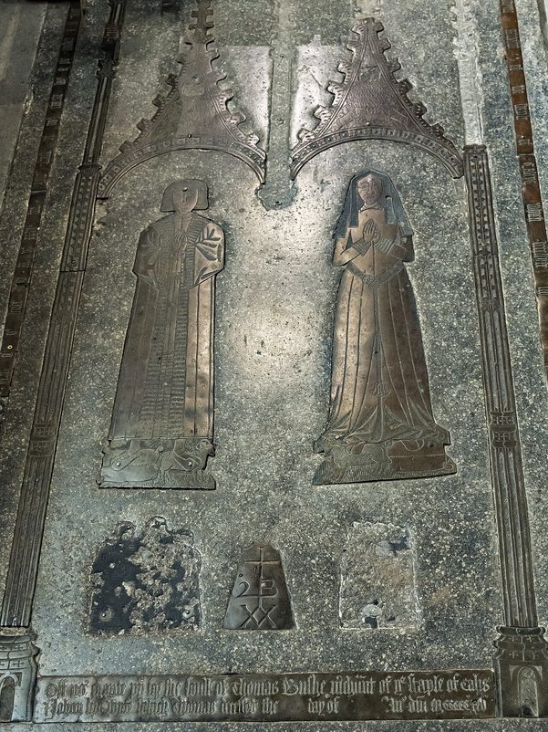 A memorial brass at Northleach of a wool merchant and his wife standing side by side, set into the stone floor