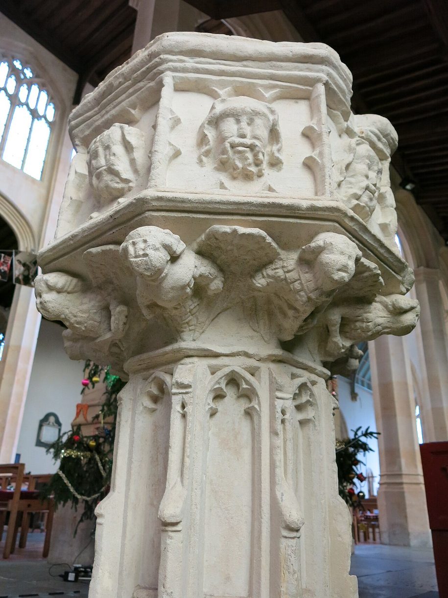 The octagonal stone font of Northleach church, its bowl carved with heads and supported by carved angels