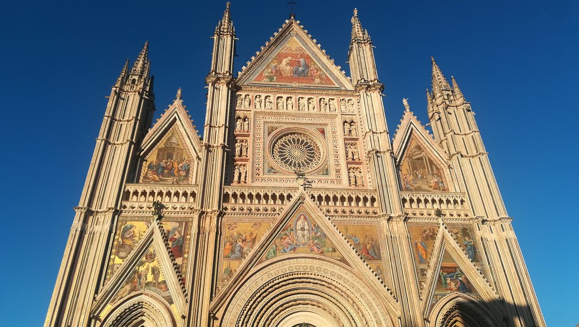 The gold mosaic facade of Orvieto Cathedral, with its three gables, spires and rose window, lit by the late sun