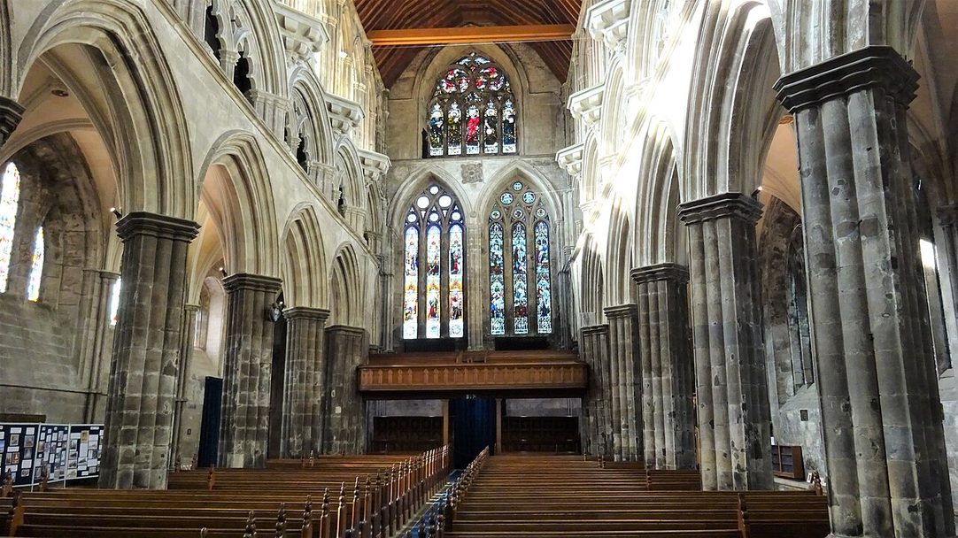 The nave of Paisley Abbey looking west, with tall pointed arcades, a triforium and clerestory, and stained glass in the west windows