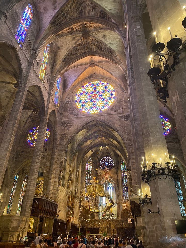 The coloured rose window seen high above the arches and columns inside Palma Cathedral