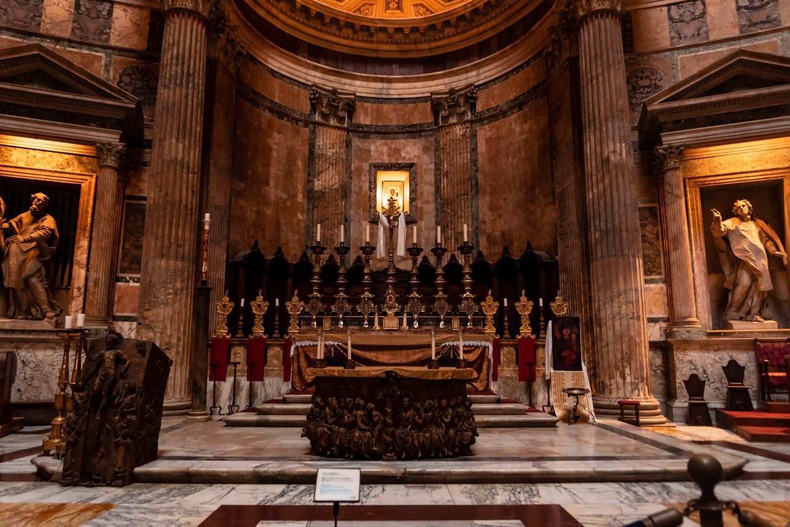 The interior of the Pantheon showing side chapels, statues and candlelight