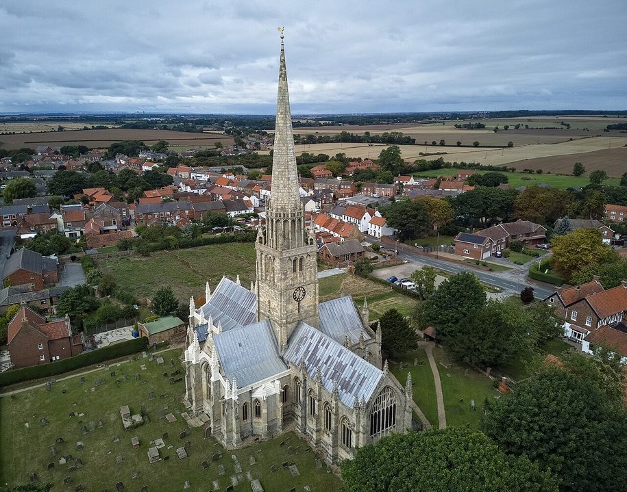 Aerial view of St Patrick's Church, Patrington, a cross-shaped church with a central spire, in the middle of the village