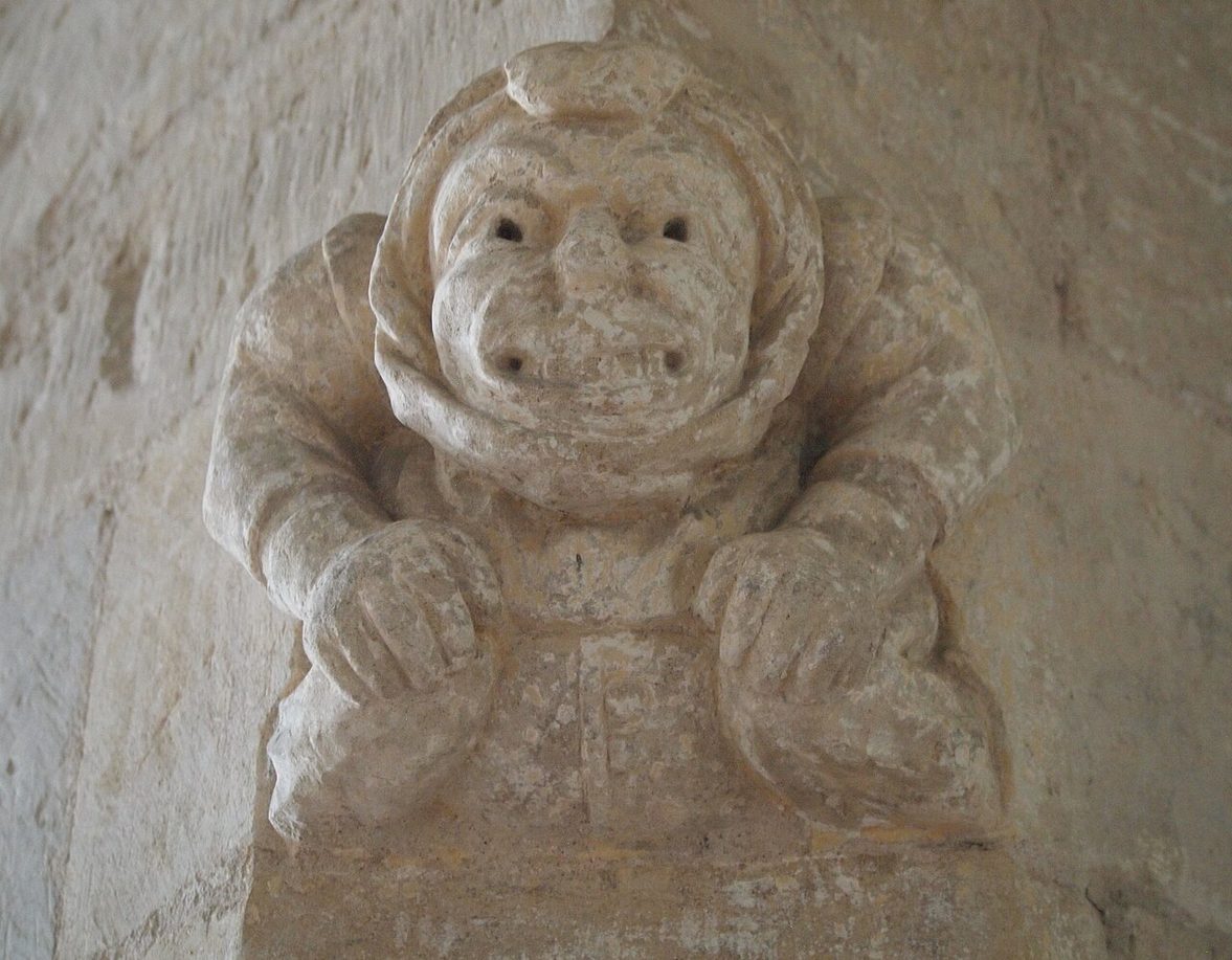 A grinning carved stone grotesque with its hands on its knees at St Patrick's, Patrington