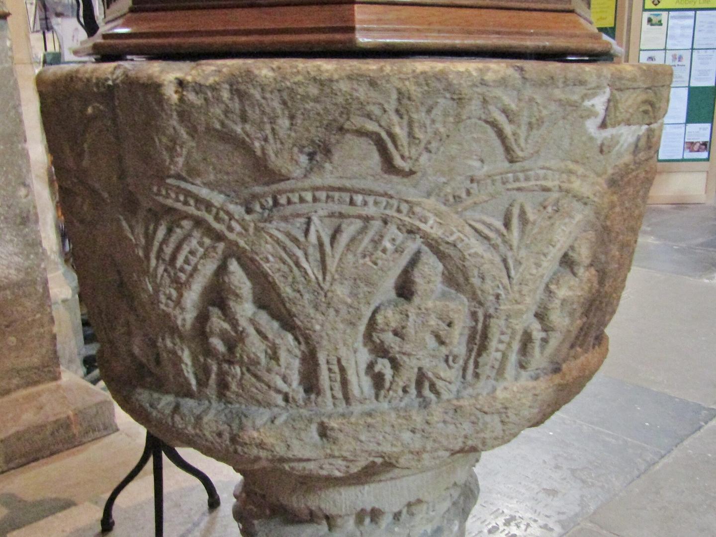 A round Norman stone font carved with arcading and figures
