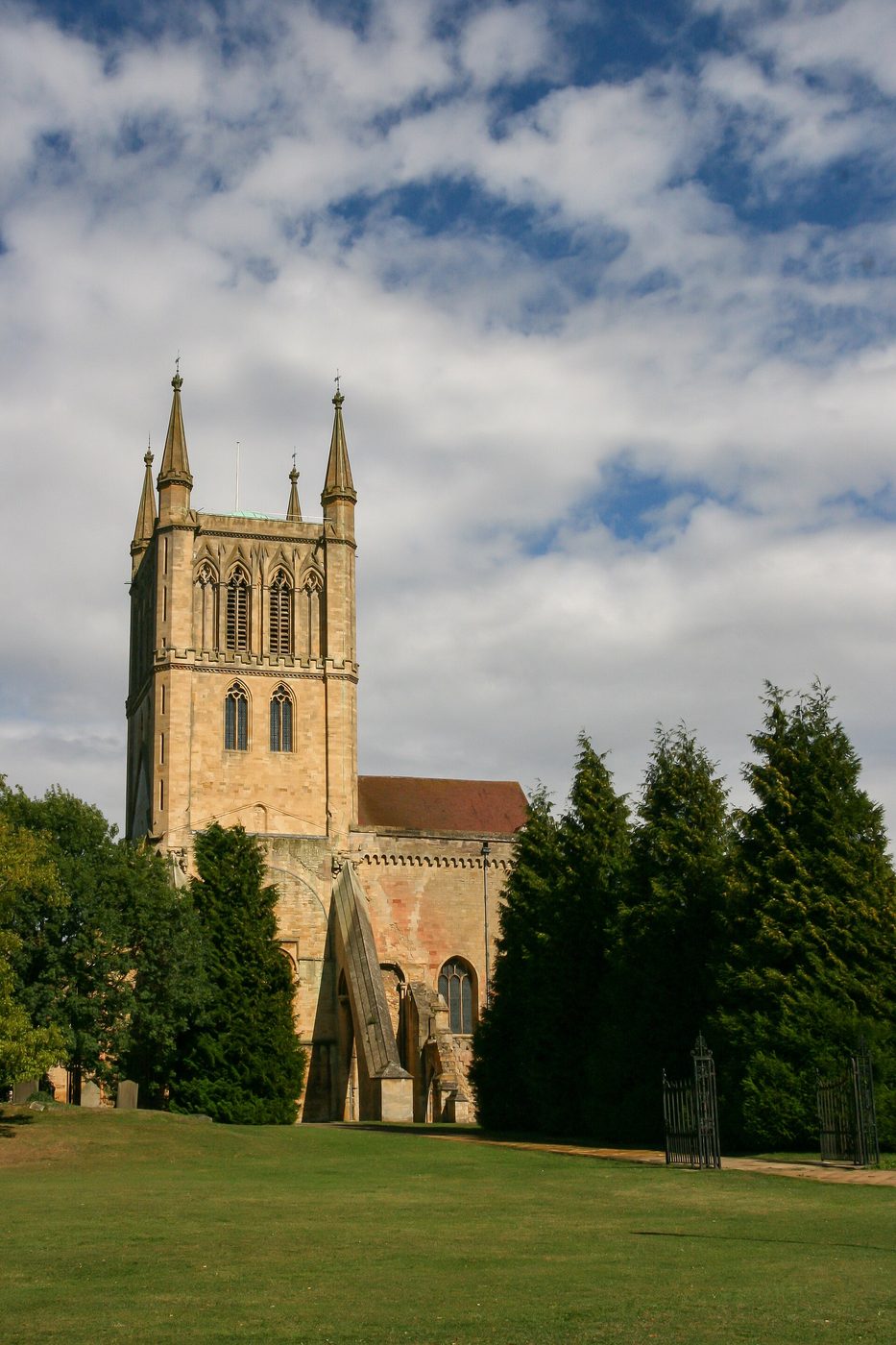 The tower of Pershore Abbey rising above trees, with tall paired openings and corner pinnacles