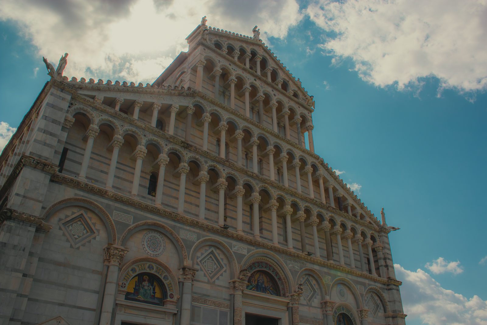 The facade of Pisa Cathedral with tiers of small arcades in white marble against a blue sky
