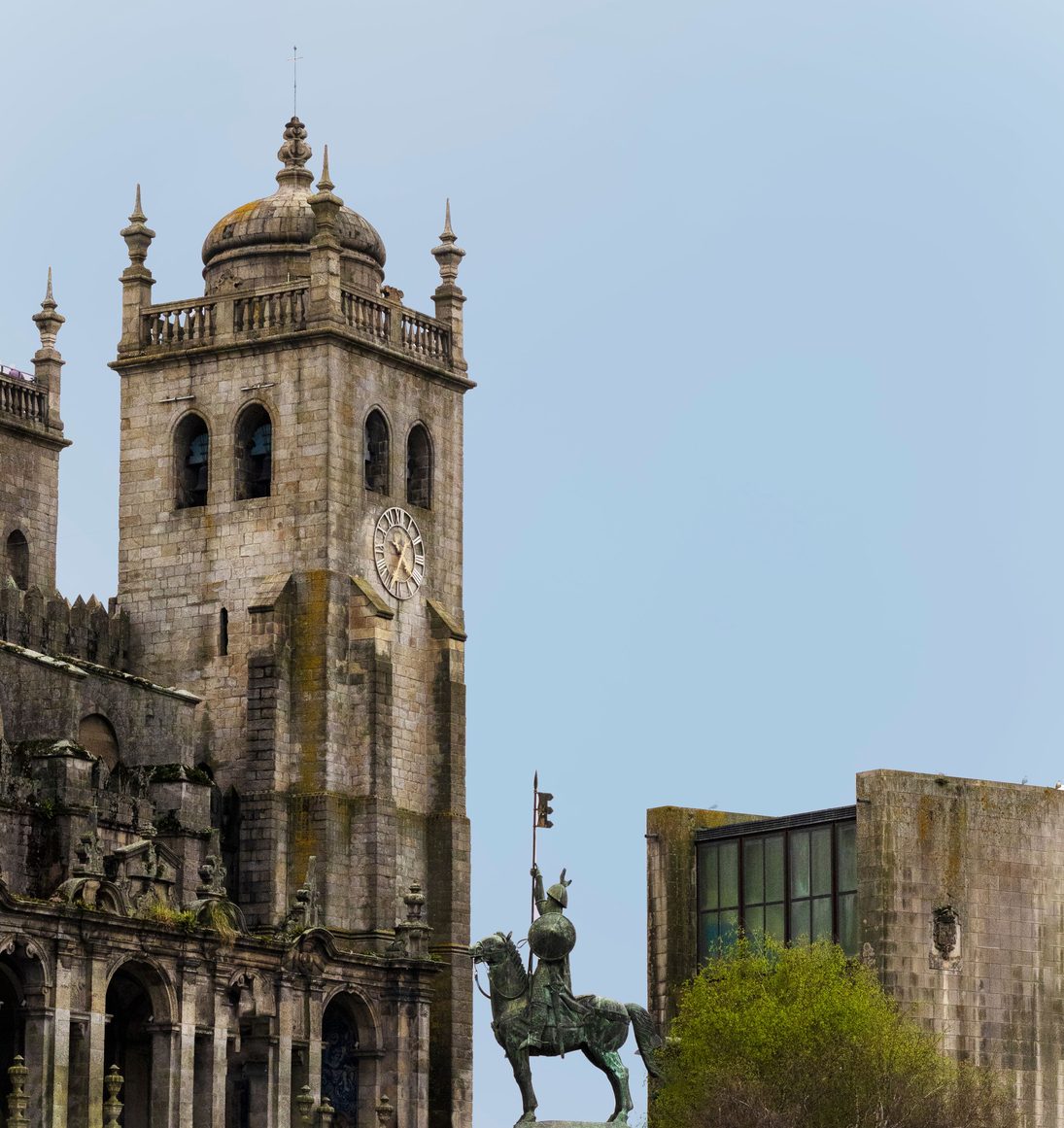A bronze equestrian statue in front of the domed tower of Porto Cathedral