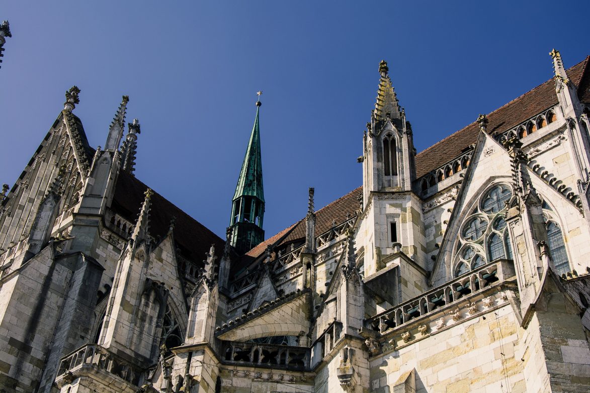 Looking up at the pinnacles, buttresses and tracery of the south side of Regensburg Cathedral against a blue sky