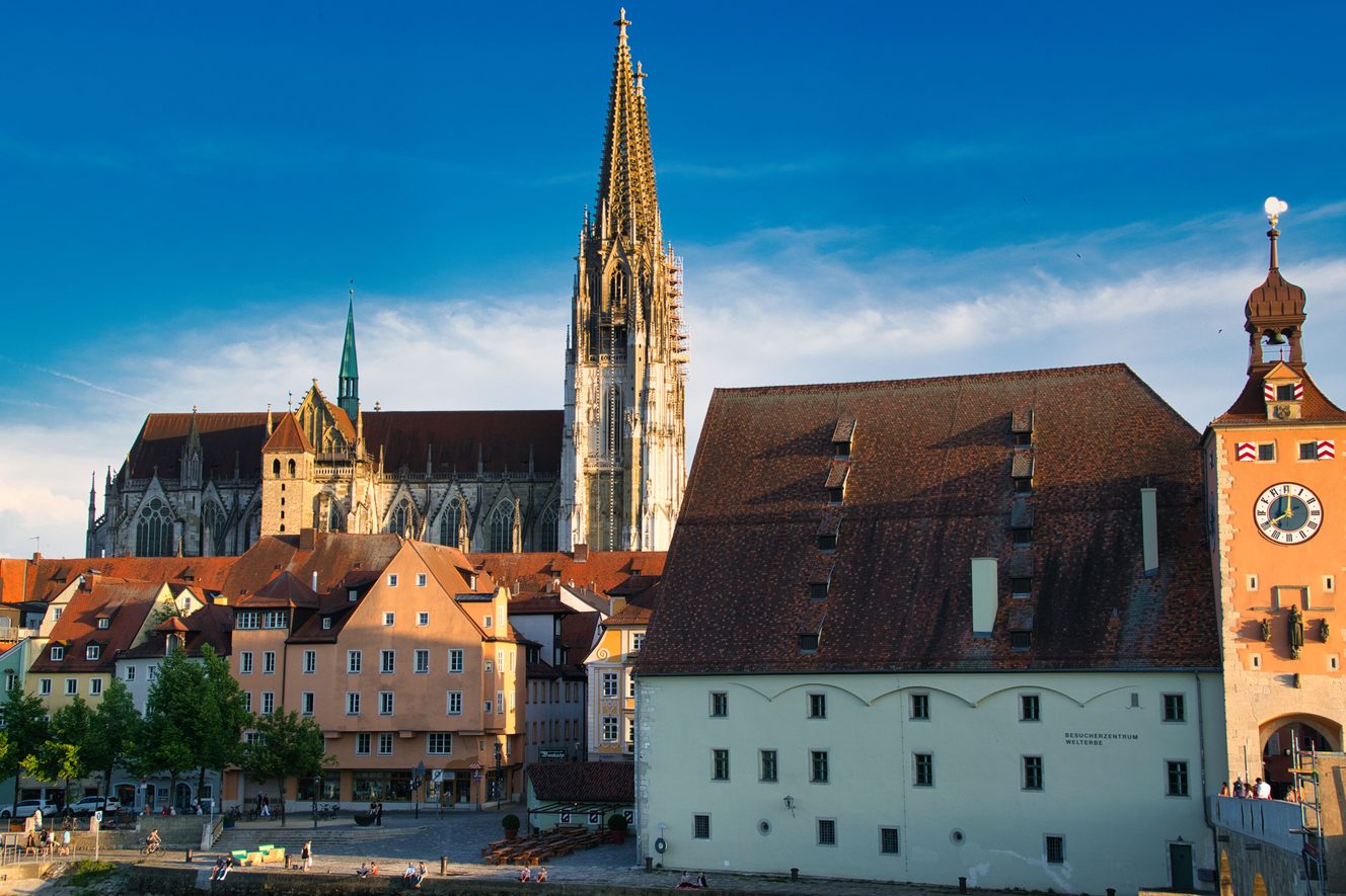 The twin openwork spires of Regensburg Cathedral rising behind the old town and the medieval bridge tower on the Danube
