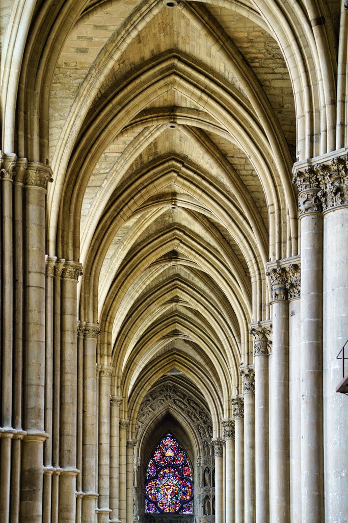 The tall Gothic arcade of an aisle in Reims Cathedral, with stained glass at the far end
