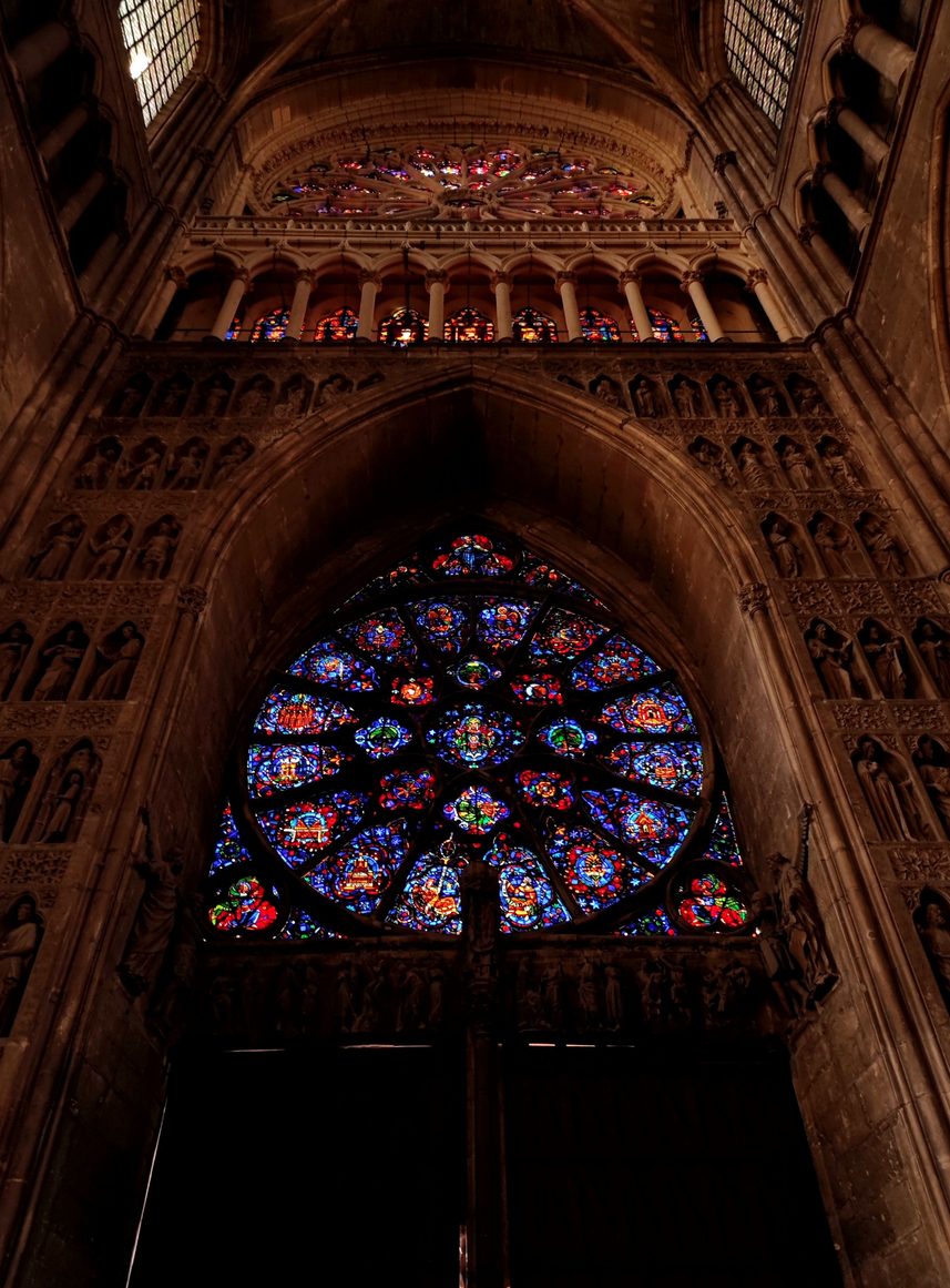 The great rose window of Reims Cathedral glowing red and blue inside the west end