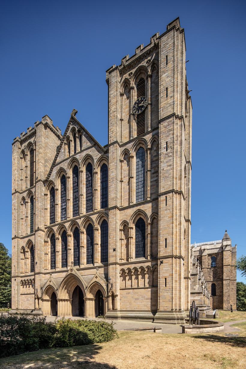 The twin-towered Early English west front of Ripon Cathedral under a blue sky