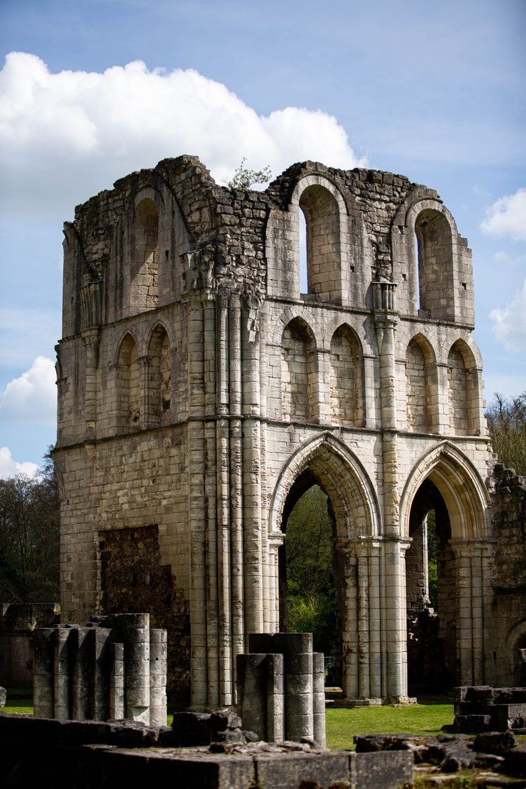 The tall ruined wall of a transept at Roche Abbey, with tiers of pointed arches against a blue sky