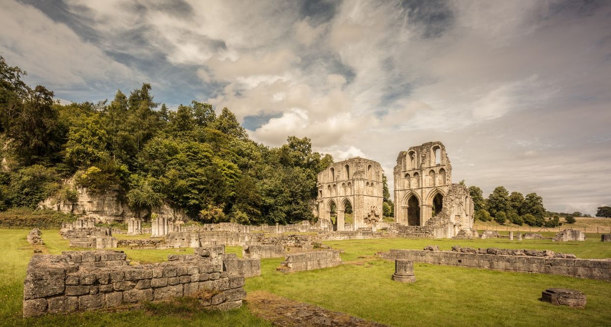 The ruins of Roche Abbey, South Yorkshire, with the two tall transept walls standing in a green valley below wooded limestone cliffs