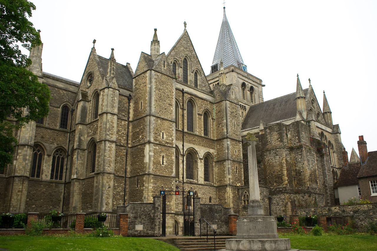 Rochester Cathedral's grey stone walls and spire seen from the green on a cloudy day
