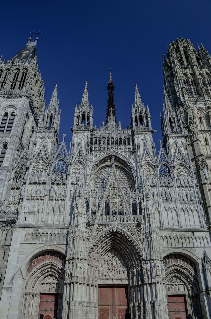 The west front of Rouen Cathedral against a deep blue sky, with its spiky gables and pinnacles