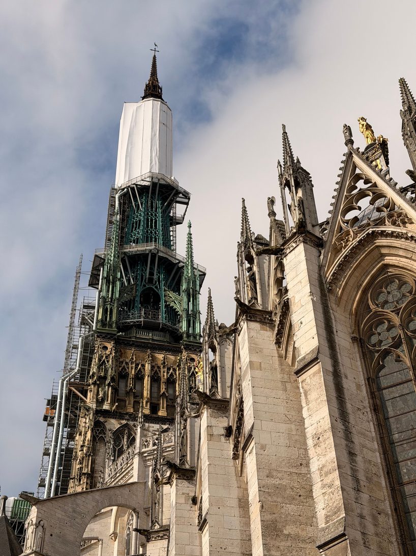 The green cast-iron spire of Rouen Cathedral under restoration, its tip wrapped in white, above the Gothic pinnacles