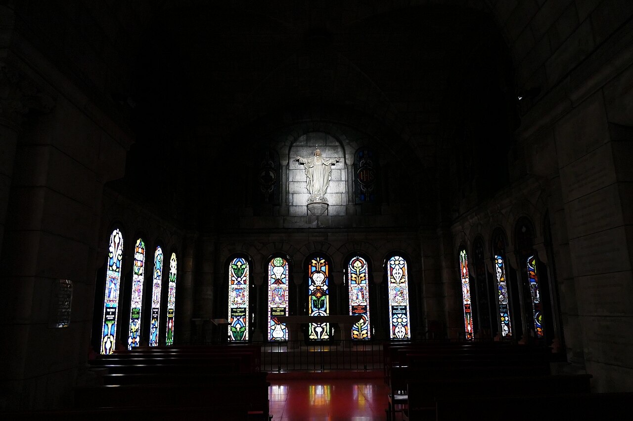 The dark crypt of Sacré-Cœur with a row of lit stained-glass windows