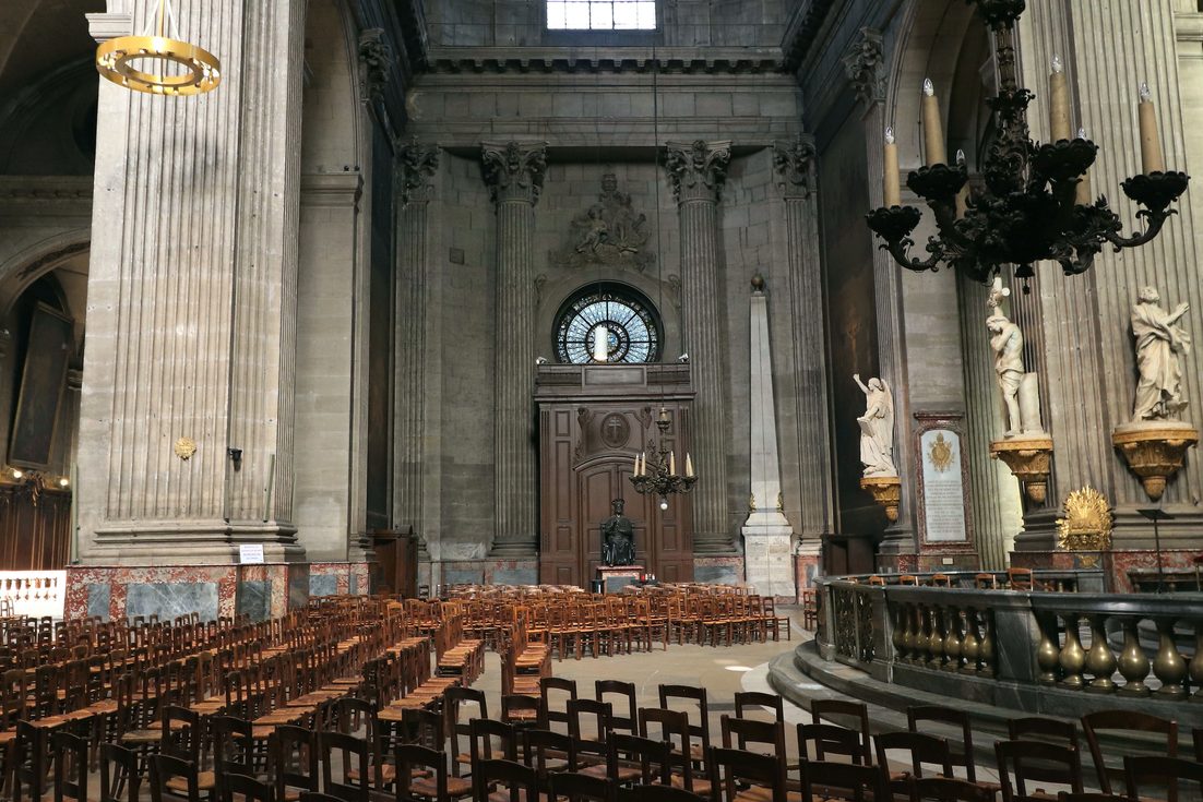 The vast pale stone interior of Saint-Sulpice with tall pillars, arches and rows of chairs