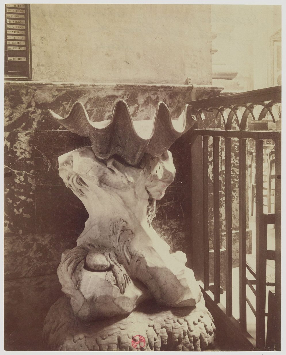 An old photograph of a giant clam shell used as a holy-water stoup on a carved rock-like base at Saint-Sulpice