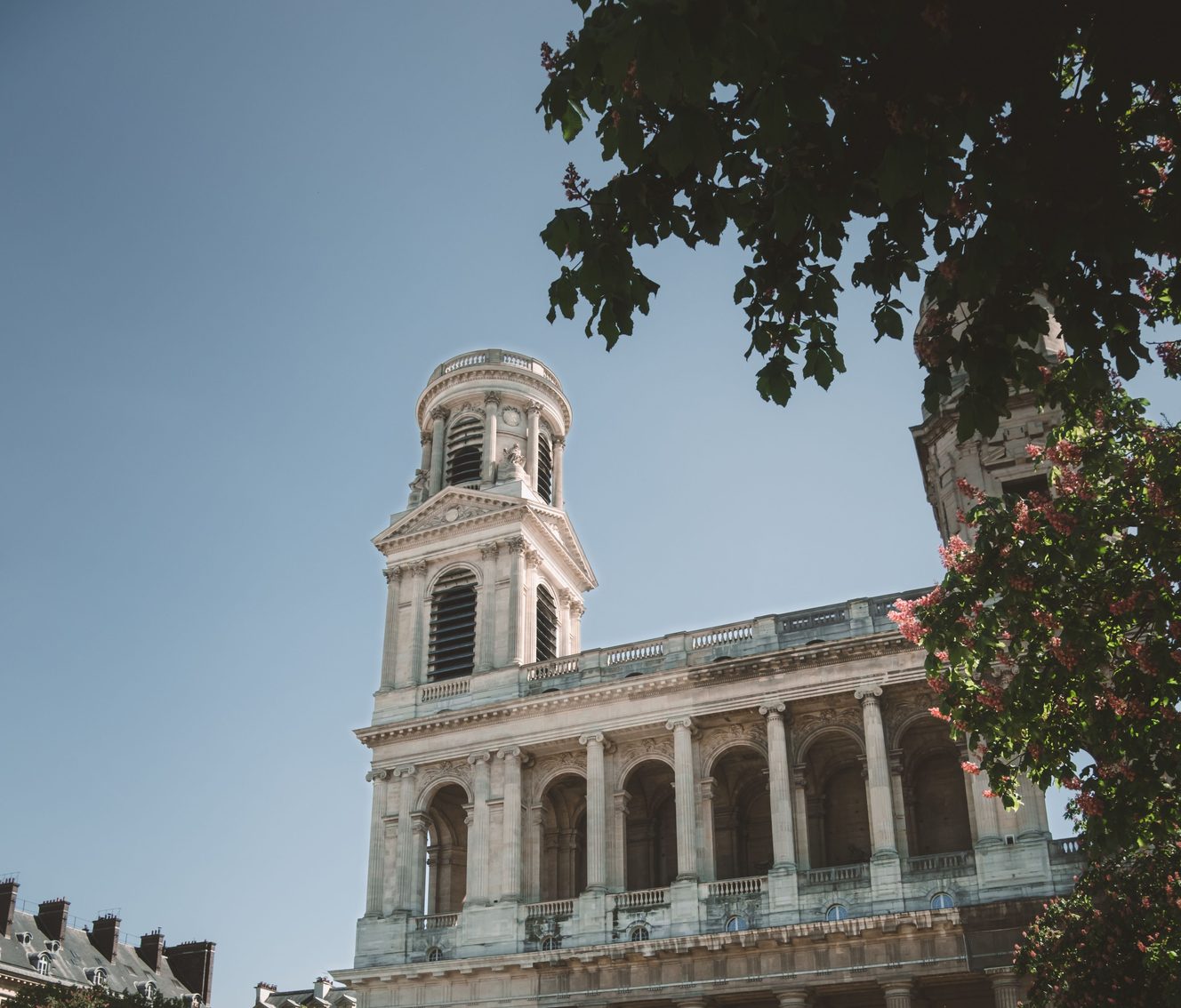 The north tower and the two-storey colonnaded facade of Saint-Sulpice in Paris, framed by trees
