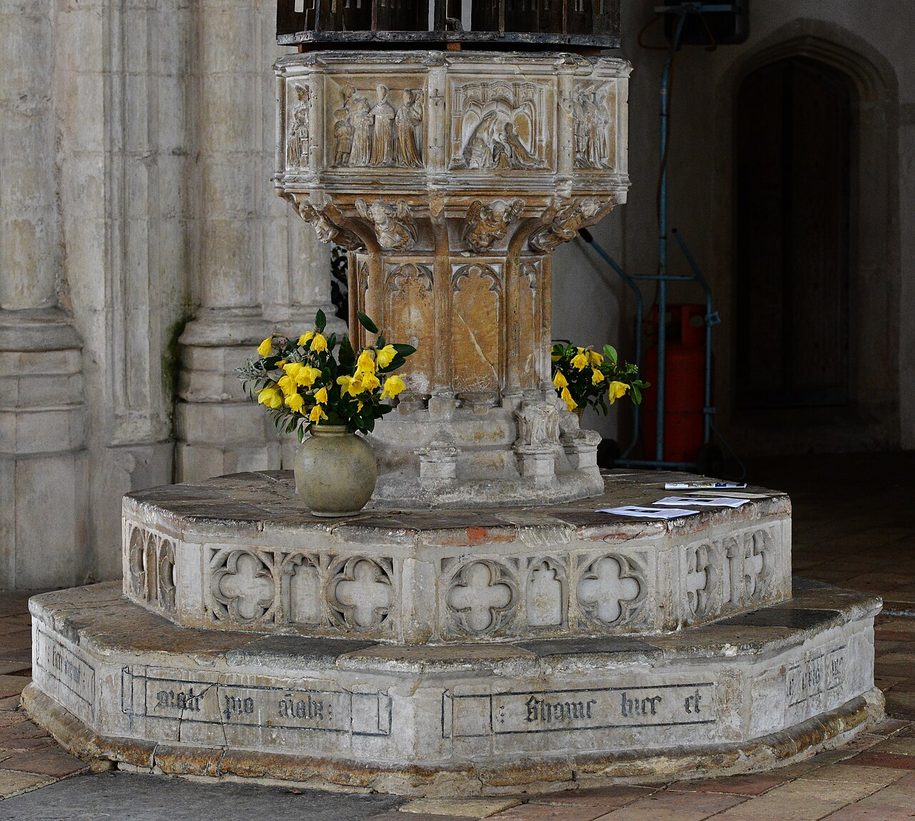 The carved stone seven-sacrament font at Salle, with a tall wooden cover hanging above it from a crane