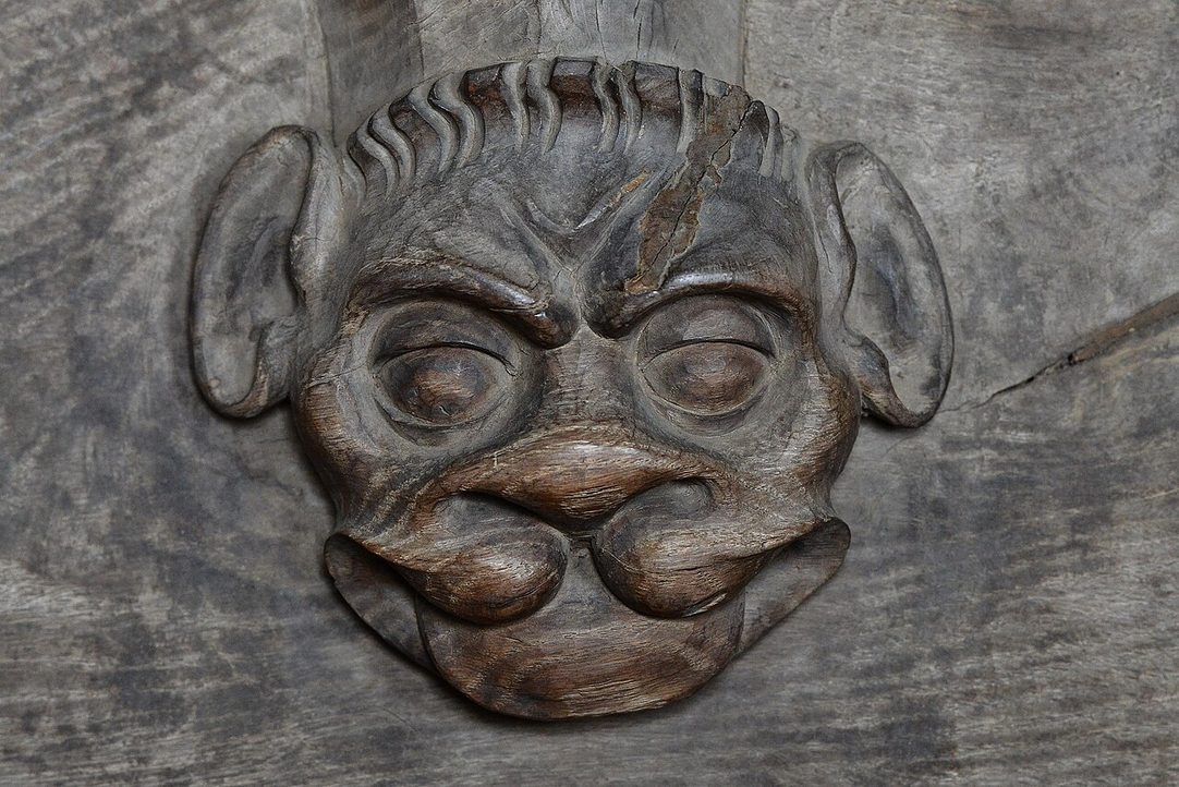 A carved wooden misericord under a choir stall at Salle, showing a grotesque face