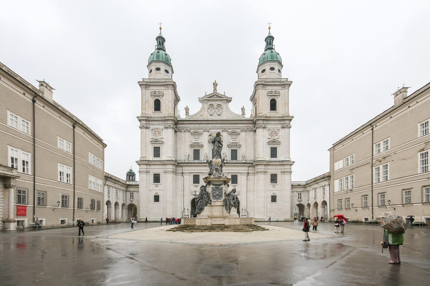 The Domplatz in Salzburg on a wet day, with the Marian column in the centre and the white facade of the cathedral behind it