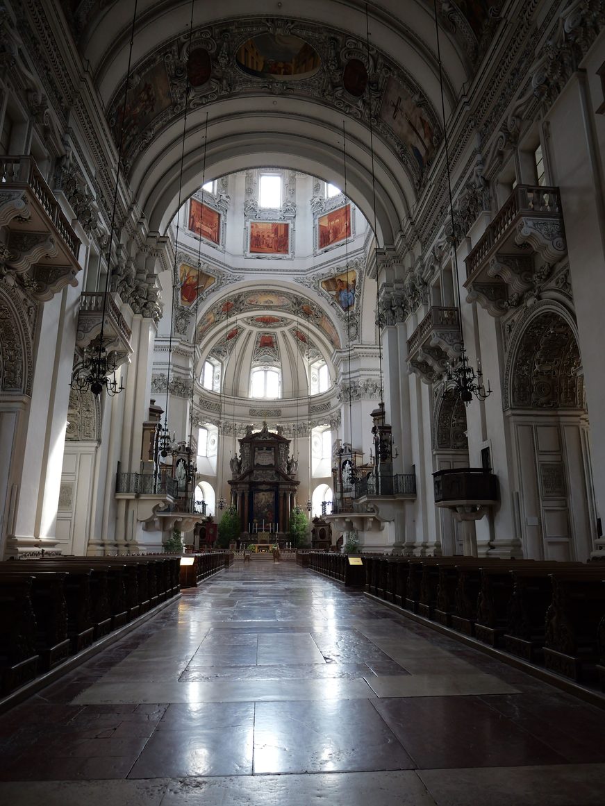 The bright white nave of Salzburg Cathedral with stucco-framed paintings on the vault, leading to the high altar under the dome