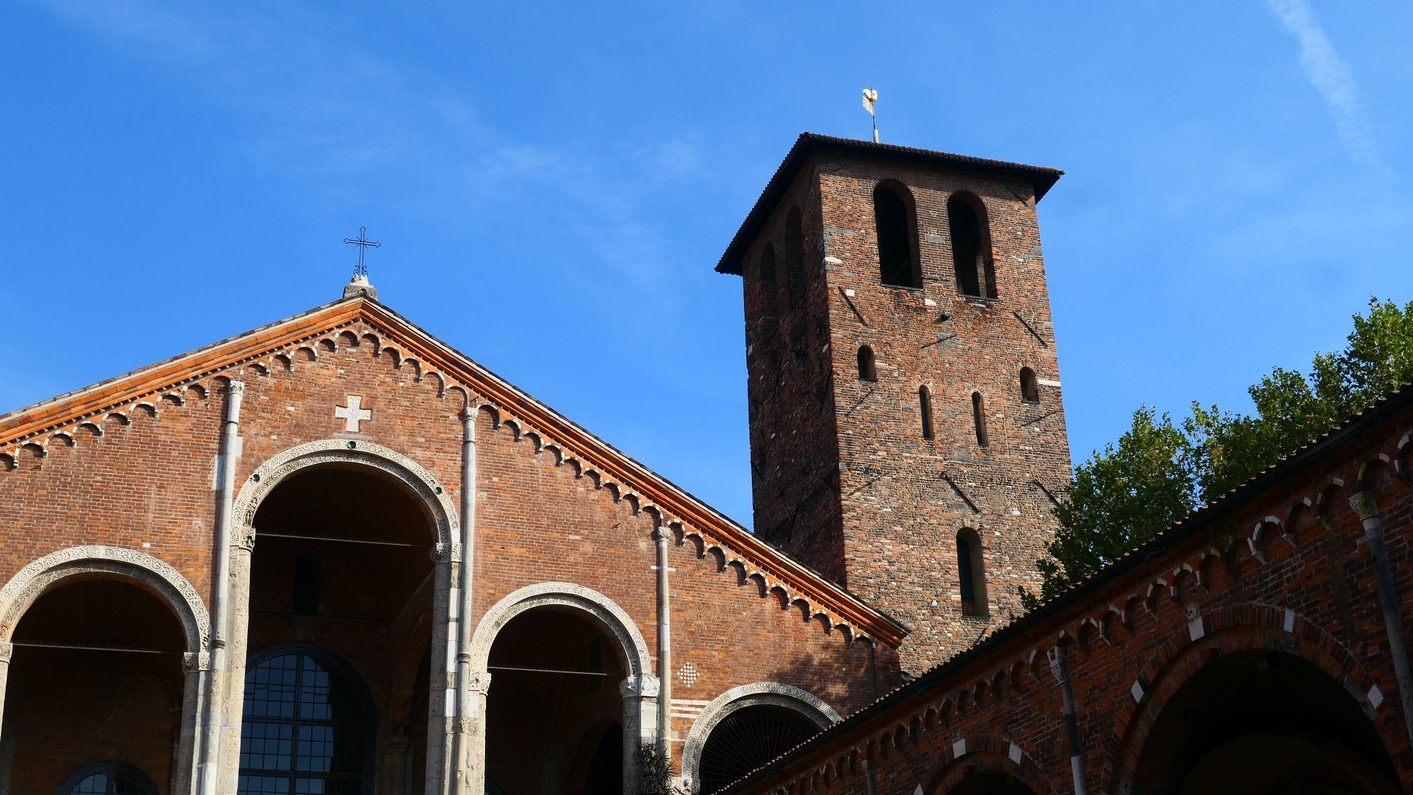 The red-brick Romanesque front of the Basilica of Sant'Ambrogio in Milan, with its loggia and tall bell tower, seen across the atrium