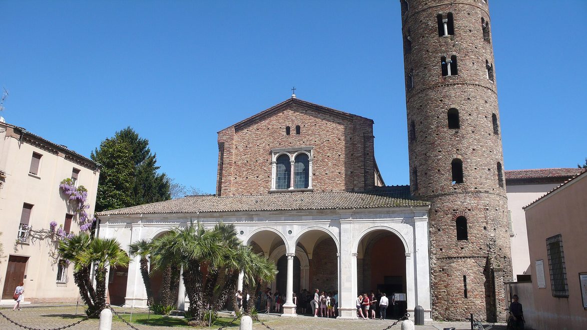 The brick front of Sant'Apollinare Nuovo in Ravenna, with its marble portico and the tall round bell tower beside it