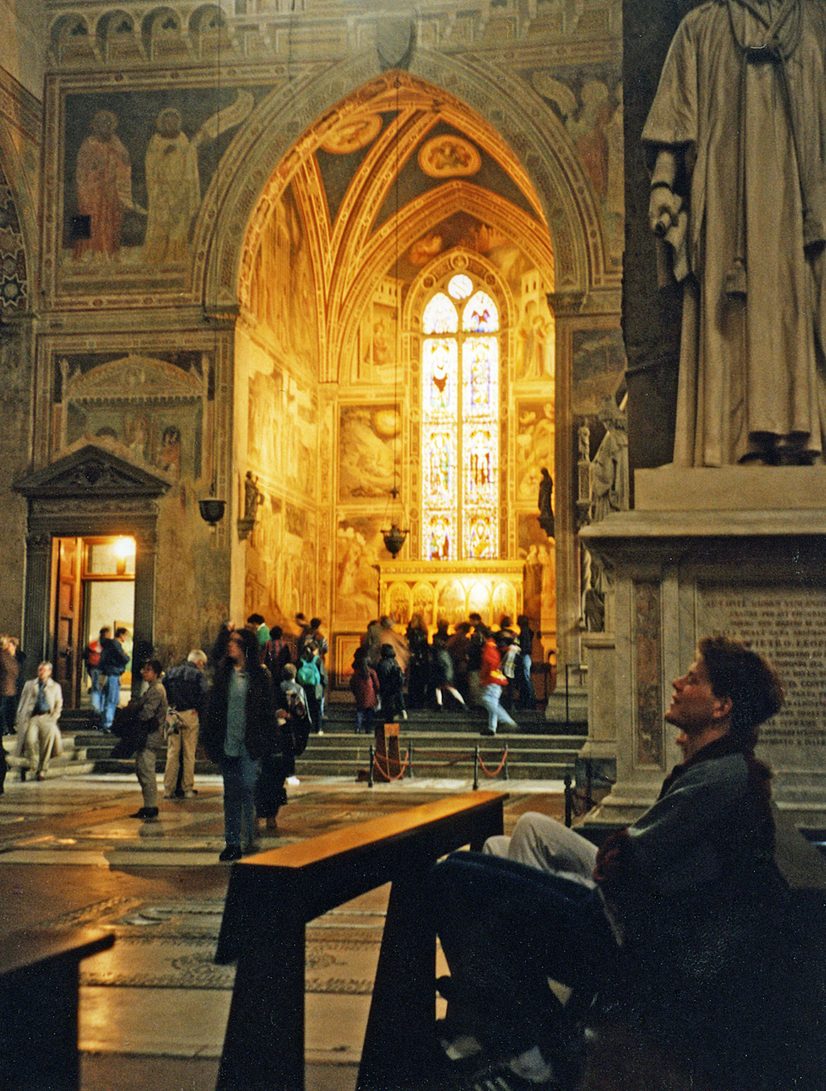 Visitors in front of a brightly lit chapel with tall stained glass windows in Santa Croce