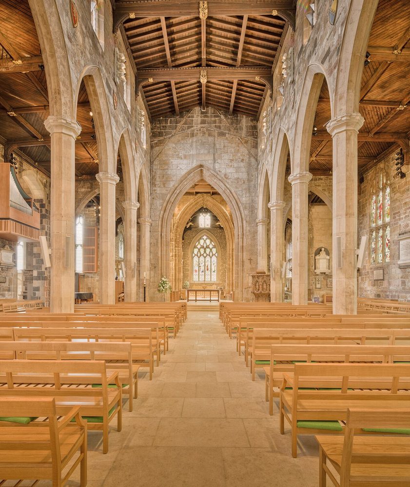 The long nave of Sheffield Cathedral with light oak benches and a level stone floor, looking east