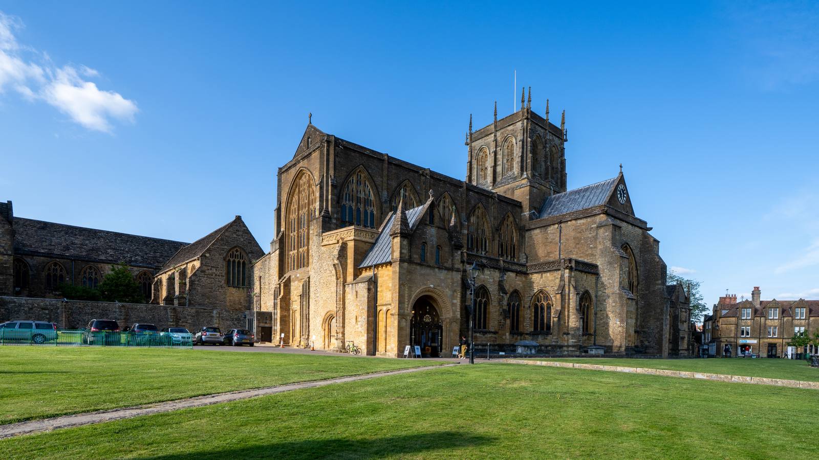 Sherborne Abbey in golden Ham stone with its central tower, seen across a lawn