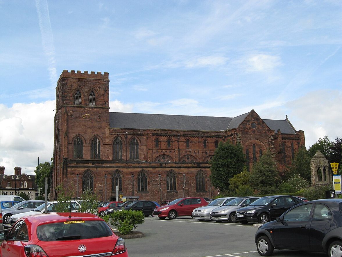Shrewsbury Abbey from the south, a long red sandstone church with a west tower and a churchyard in front