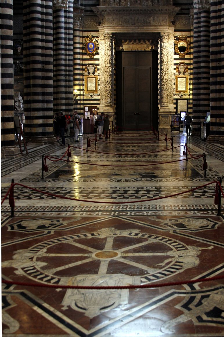 The inlaid marble floor of the nave of Siena Cathedral, uncovered, looking towards the entrance between striped columns