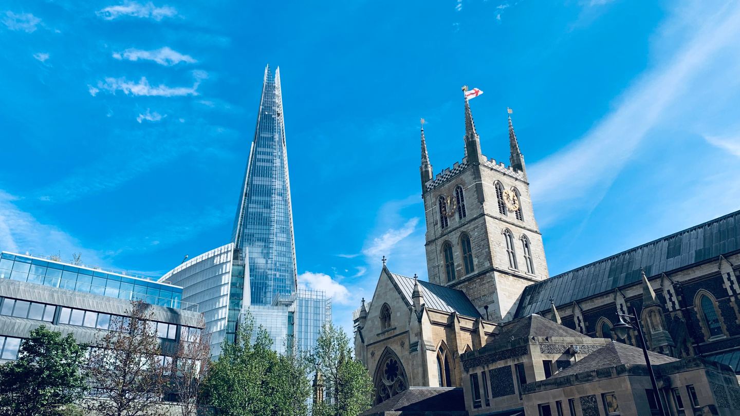 Southwark Cathedral's pinnacled tower beside the glass spike of the Shard under a blue sky