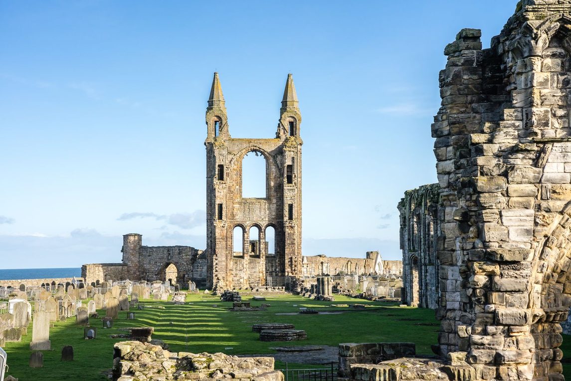 The twin-turreted east gable of St Andrews Cathedral seen along the grassed-over nave, with the sea beyond