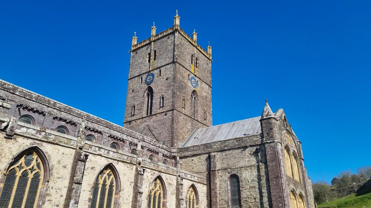 The central tower of St Davids Cathedral rising above the long roof of the nave against a blue sky