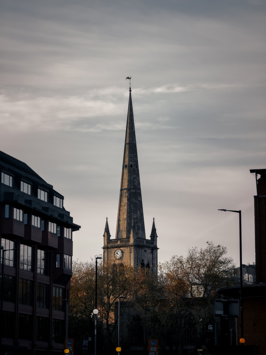 The tall stone spire of St Mary Redcliffe rising above the buildings of a Bristol street